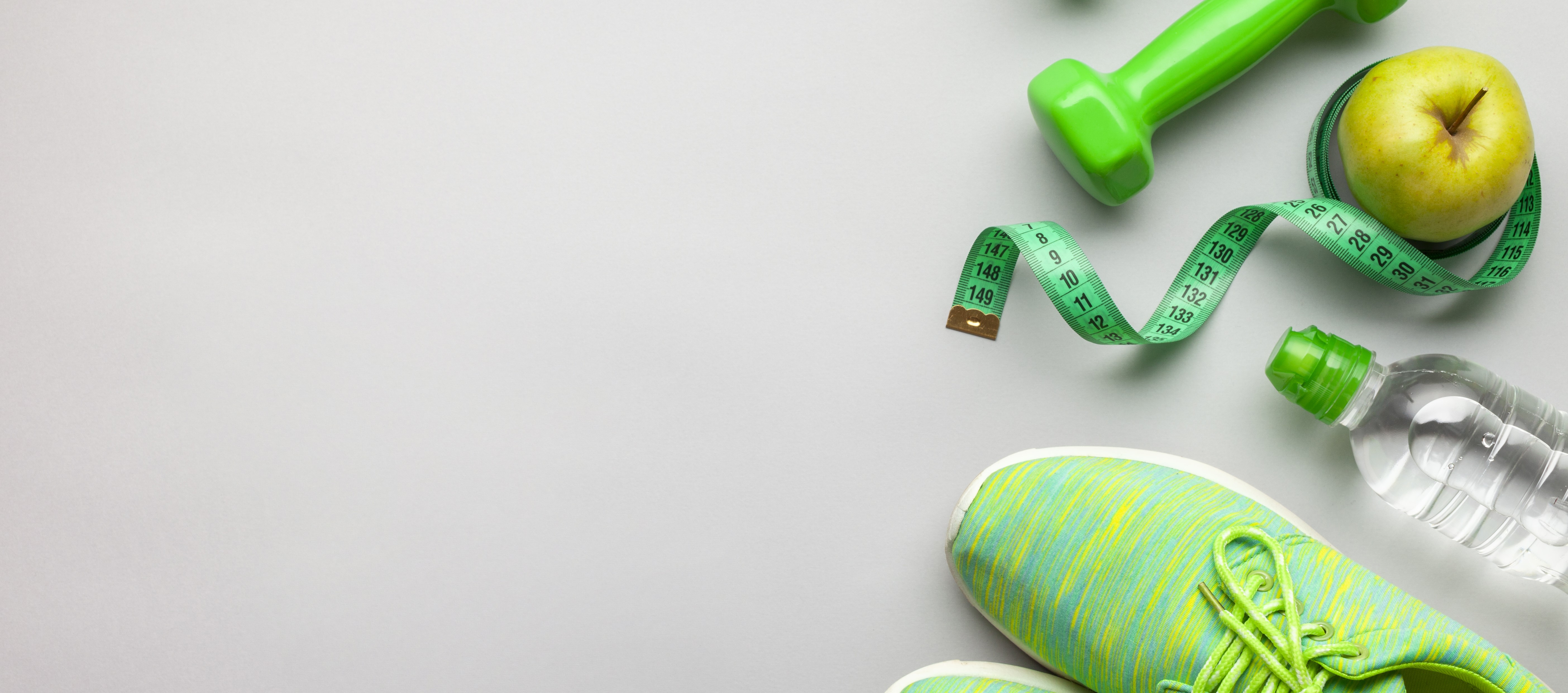 Grüne Laufschuhe, grüne Hanteln und Trinkflasche. Grüner Apfel mit Maßband